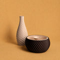 Shell & Seed and Spiral Vase bundle featuring an brown ribbed Shell & Seed piece with an ivory interior alongside an ivory spiral-textured vase on a warm textured background.